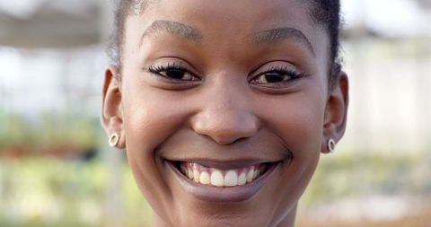 Woman smiling in greenhouse setting surrounded by lush foliage