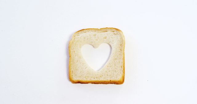 A slice of bread with a heart-shaped hole cut out of the center is presented against a white background, with copy space. It symbolizes love for food or could be used in a concept related to healthy eating habits.