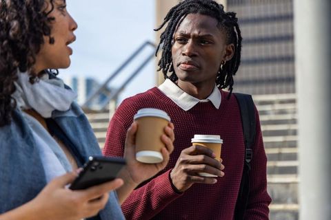 Young professionals holding coffee, chatting on city stairs with backpack and smartphone