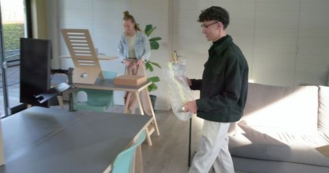 Diverse coworkers unpacking and carrying floor lamp in bright modern open-plan workspace