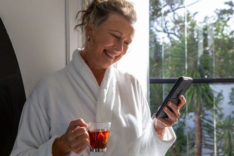 Senior Woman Relaxing at Home Using Smartphone and Enjoying Tea