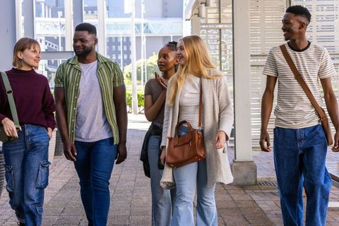 Multiracial friends walking and chatting on urban walkway, casual young adult lifestyle