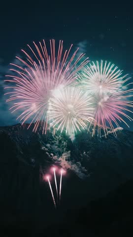 Launching fireworks over mountain valley at night, vertical spectacle with aerial shells