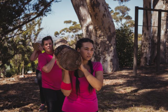 Group of women participating in an outdoor boot camp, carrying a heavy wooden log as part of an obstacle course. Ideal for use in fitness and health promotions, team-building activities, and outdoor adventure advertisements.