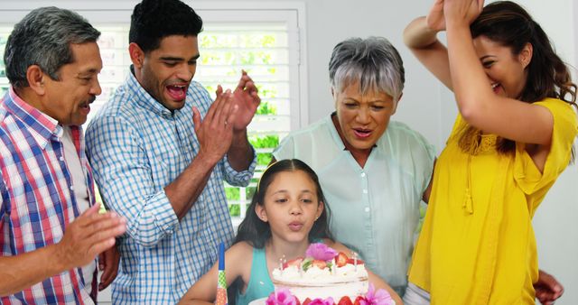 Biracial daughter blowing out candles on birthday cake with cheering parents and grandparents. Celebration, party, birthday, childhood, family, togetherness, domestic life and lifestyle, unaltered.