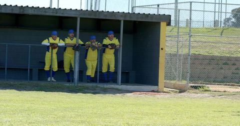 Senior baseball teammates leaning on dugout railing in bright yellow uniforms under sunlight