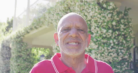 Senior Man Smiling in Sunlit Garden with Vibrant Foliage