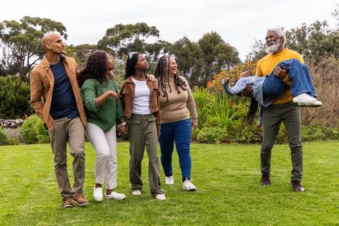 Multigenerational diverse family walking and laughing while granddad carries child in garden