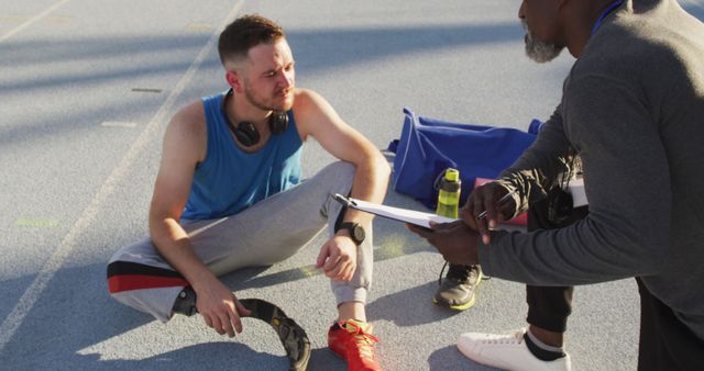 Athlete sitting on outdoor track listening to coach's instructions. Ideal for illustrating coaching, mentoring, fitness guidance, outdoor sports training, and teamwork concepts.