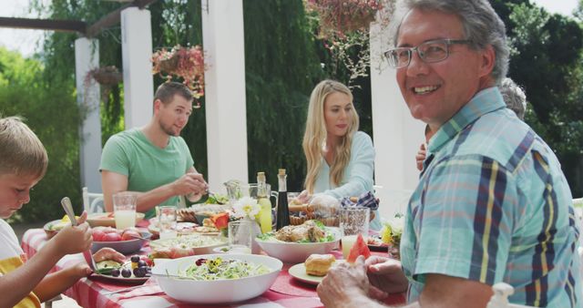 Happy caucasian family sitting at table in garden, eating dinner. Lifestyle, domestic life, family, and togetherness.