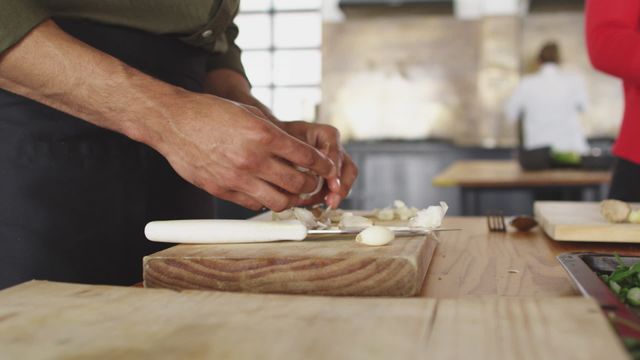 Chef skillfully prepares ingredients on a chopping board using knife skills in a modern kitchen environment. Suitable for use in articles or advertisements on culinary arts, professional cooking, or cooking classes. Highlights the expertise and precision required in professional kitchens.