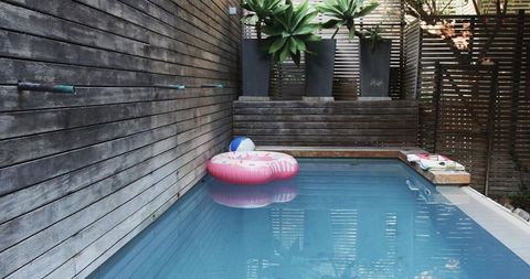 Minimalist backyard reflecting blue pool with pink donut float, beach ball and wood planters