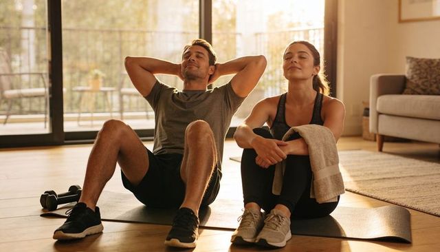 Couple cooling down after home workout relaxing on mats during post-exercise recovery