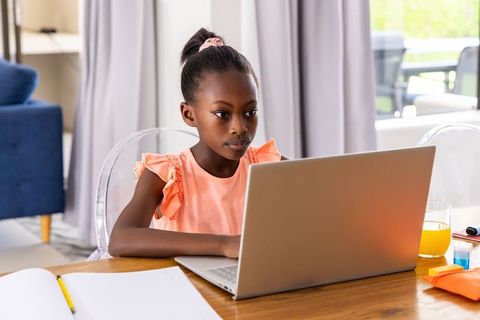 African girl studying on laptop for remote learning with notebook and orange juice
