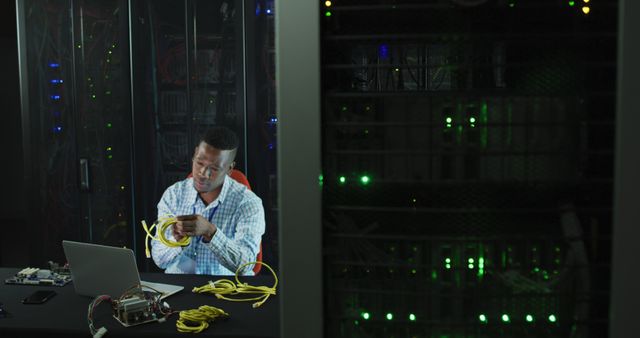 Network engineer is handling cables in dimly lit data center with servers. Ideal for illustrating concepts in network management, data security, and IT professional roles. Suitable for articles, training material, and educational content about information technology and hardware maintenance.