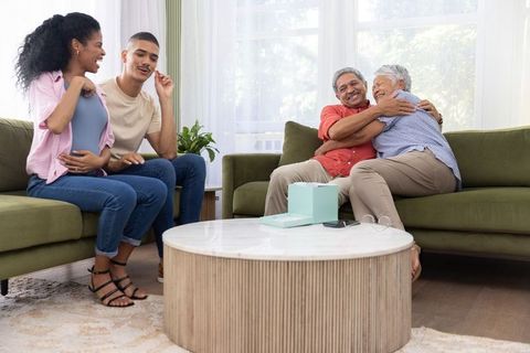Multigenerational family celebrating pregnancy with grandparents hugging in sunlit living room