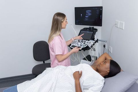 Female sonographer performing abdominal ultrasound with african american patient on bed