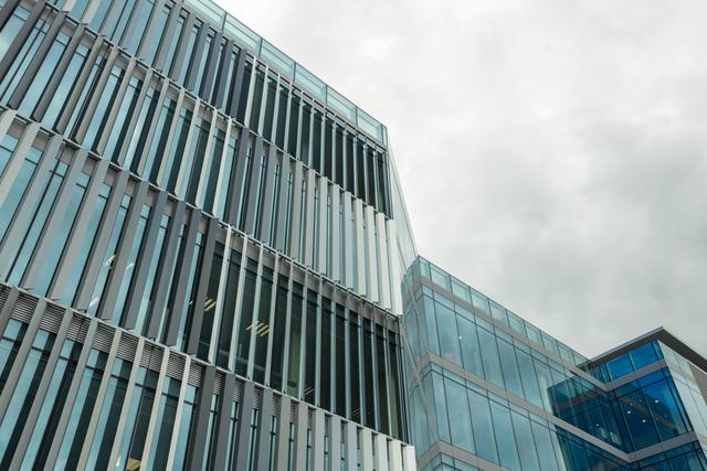 Low angle view of a modern office building with a glass facade against a cloudy sky. Ideal for use in corporate presentations, real estate marketing, architectural portfolios, and urban development projects.