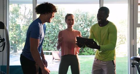 Group of Friends Laughing at Tablet in Sunlit Living Room