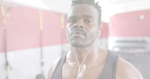 Intense sweating man training with wired earphones trx gym closeup determination
