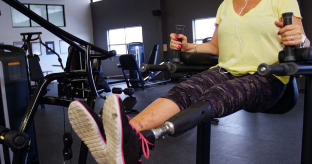 Woman seated on gym machine, holding handles, listening to music on earphones. Ideal for illustrating themes of fitness, health, and motivation. Useful for websites, fitness blogs, and promotional materials related to exercise and wellness.