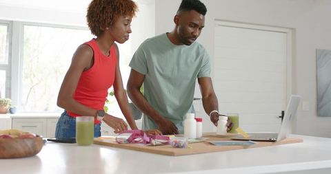 Diverse couple reviewing supplements and laptop on modern kitchen island, health planning