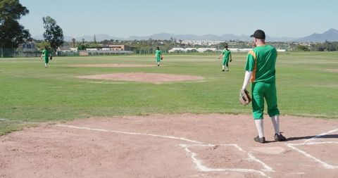 Mature baseball player standing in batter's box holding glove on sunny grass field