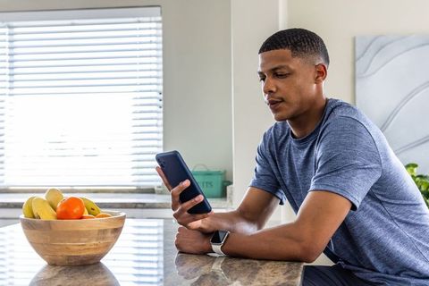 African american man checking phone while leaning on modern kitchen counter with fruit