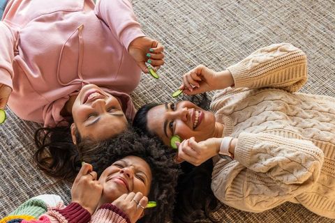 Three friends lying on rug enjoying at-home spa night with cucumber slices and laughter