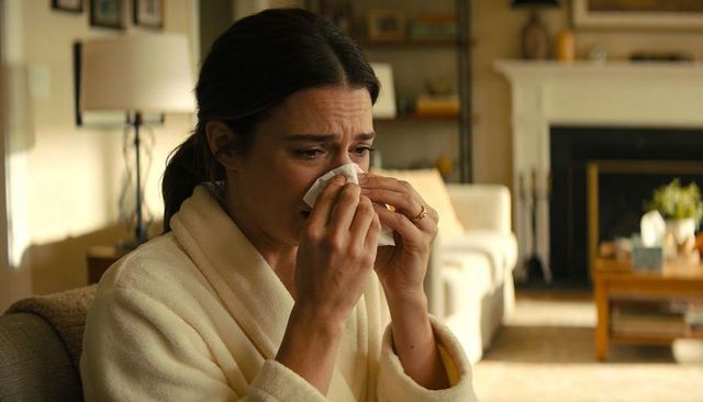 Middle-aged woman crying on couch wiping face with tissue in cozy living room