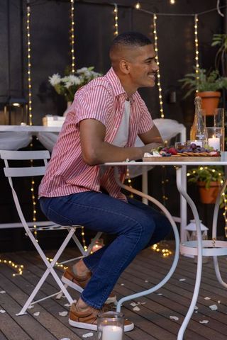 Smiling man leaning at candlelit outdoor dinner table with charcuterie and string lights