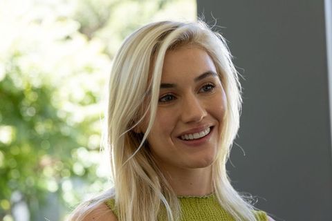 Smiling blonde woman wearing green knit sleeveless top by sunlit window bright lifestyle portrait