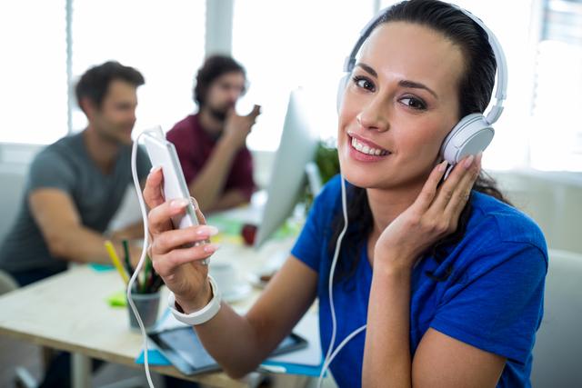 Female graphic designer enjoying music through headphones while working in a modern office. Ideal for depicting a relaxed and creative work environment, promoting workplace wellness, or illustrating the use of technology in professional settings.