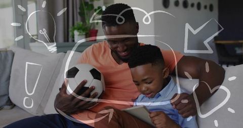 Father and son sharing tablet while holding soccer ball on couch