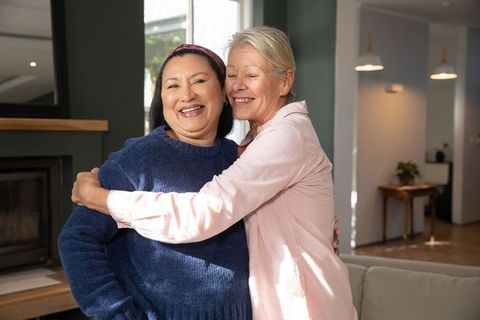Diverse senior female partners embracing in sunlit living room, affection and companionship