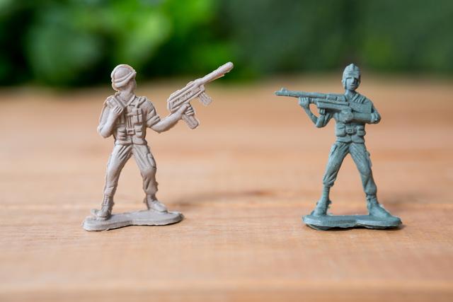 This image shows two miniature army soldiers in battle poses on a wooden surface. One soldier is beige, and the other is green, both holding rifles. Ideal for use in articles or advertisements related to childhood toys, military-themed games, or hobby collections. Can also be used in educational content about military history or strategy games.