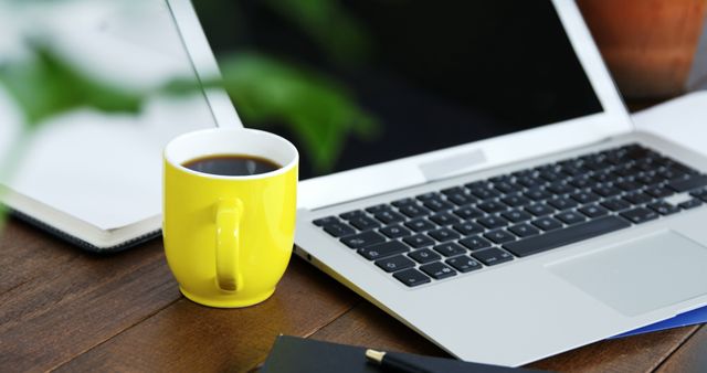 Bright yellow coffee mug next to laptop in modern workspace evokes productivity and focus. Useful for illustrating remote work, home office setup, freelance utility, or digital projects. Appeals to themes of efficiency, professional environments, and comfortable working conditions.