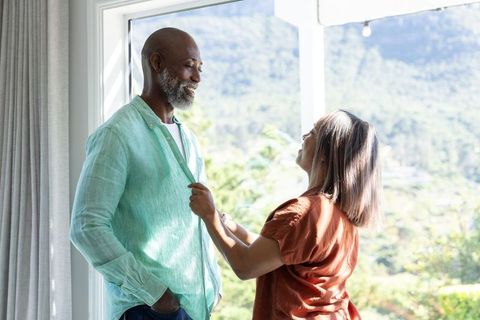 Mature couple sharing tender moment near sunlit patio, woman adjusting man's shirt