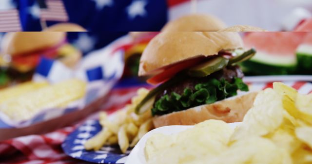 A classic American-style hamburger with chips is prominently displayed on a plate adorned with stars, with copy space. Patriotic elements like the American flag in the background suggest a celebration such as the Fourth of July or Memorial Day.