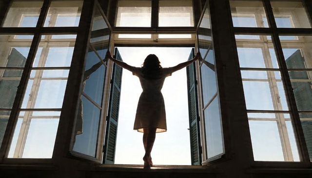 Silhouette woman opening large french shutters on window sill, backlit morning light