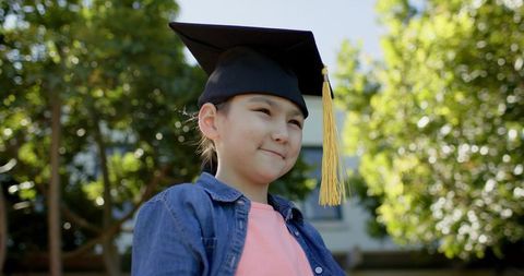 Smiling girl wearing mortarboard with yellow tassel outdoors celebrating graduation