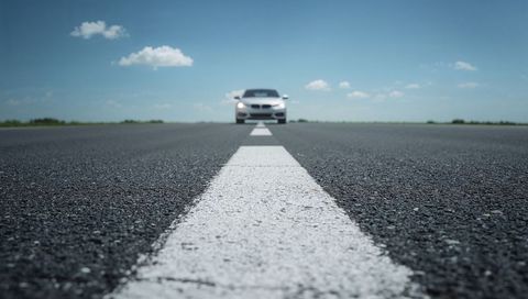 Low-Angle Driving White Sedan Heading Toward Viewer on Open Asphalt Road