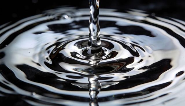 Macro water stream forming central column and concentric ripples with reflective rings