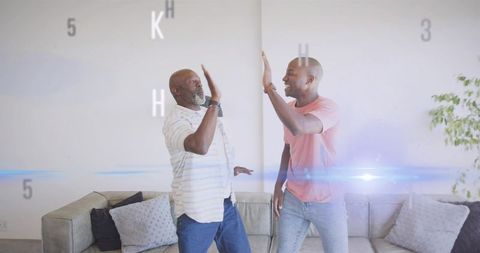 Older man and younger man high-fiving in bright living room sharing joyful family bonding