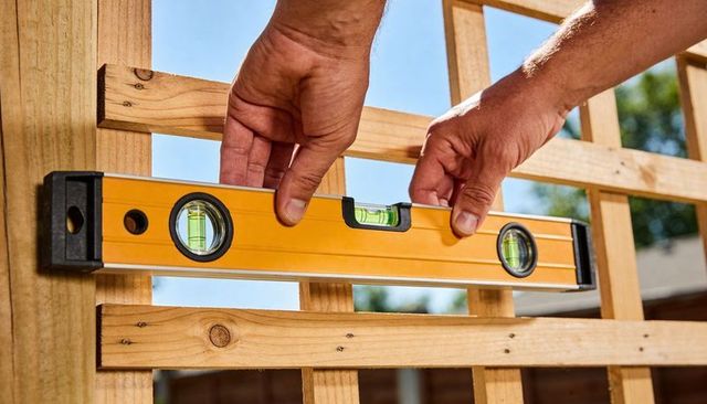 Contractor measuring wooden lattice with yellow spirit level for precise outdoor carpentry