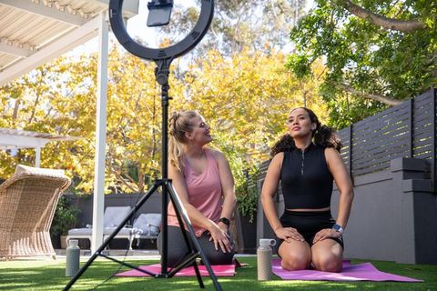 Diverse women filming outdoor yoga session with ring light