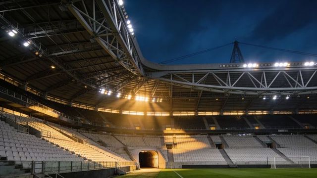 Empty modern stadium under golden floodlights at twilight with illuminated player tunnel