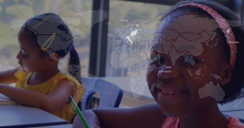 Smiling schoolgirl holding green pencil in classroom with dotted world map overlay