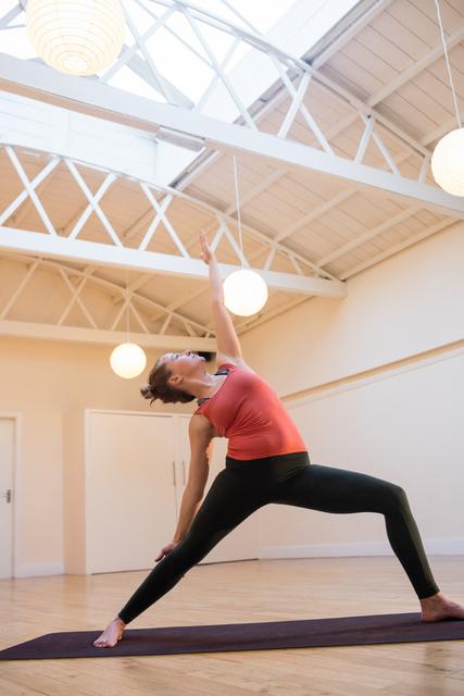 Woman performing triangle pose on exercise mat in fitness studio