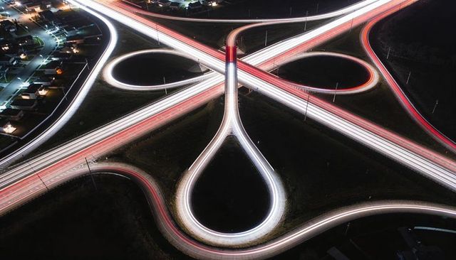 Overhead night cloverleaf interchange showing looping ramps and long exposure light trails